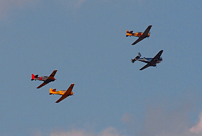 [Four colorful small planes flying away from the camera. One is red and silver, two are yellow, and the fourth is silver.]